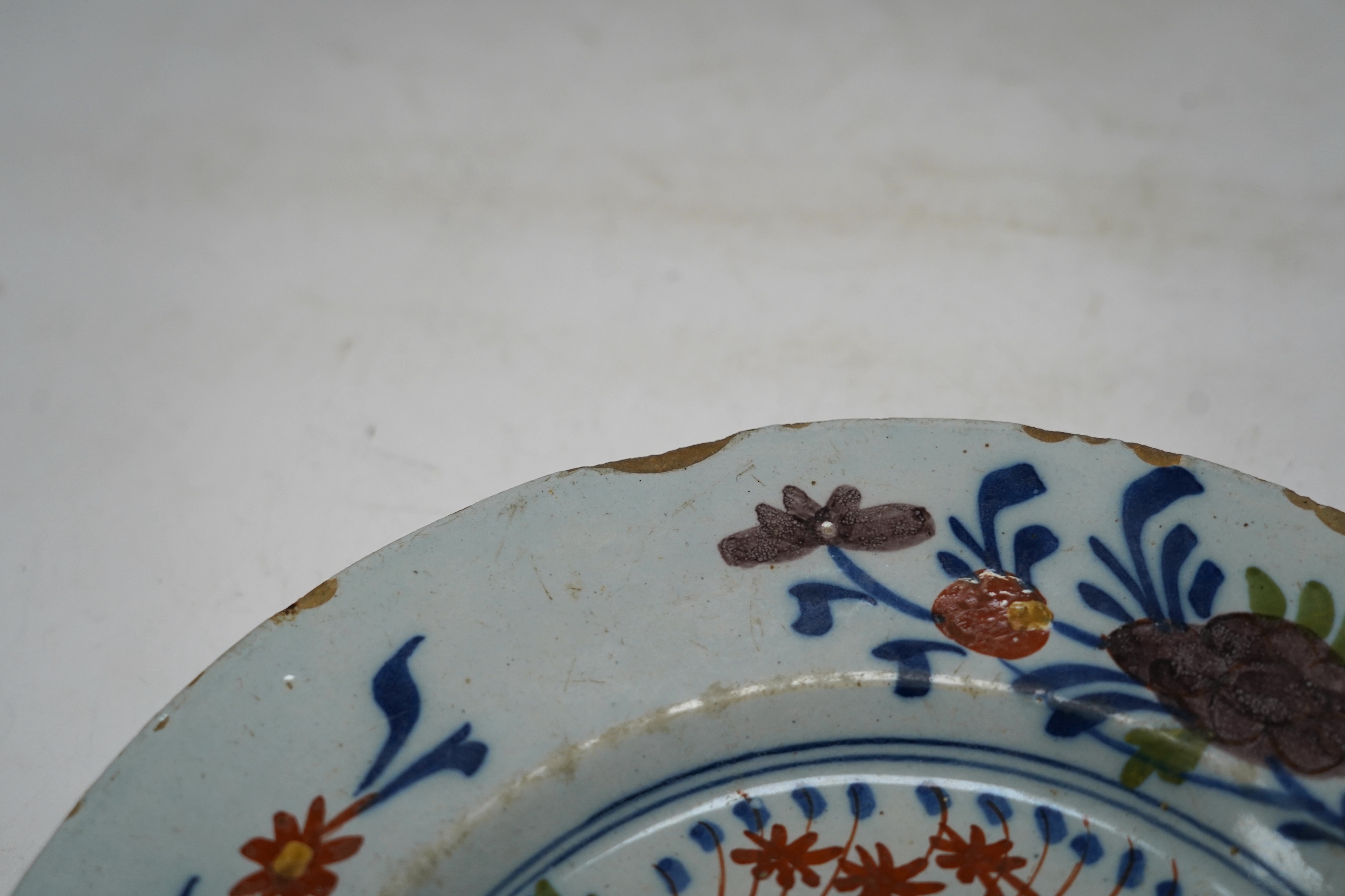 An 18th century Delft polychrome plate, 23cm diameter, and two framed tiles. Condition - tiles poor, plate with usual chipping to edges